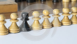 Chess pawns stand in a row, one black, many white