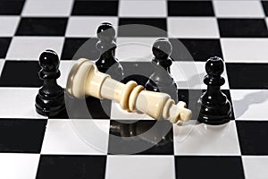 Chess is photographed on a chessboard. White pawns surrounded the defeated black queen on the chess table