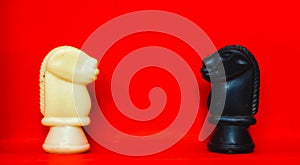 Chess pieces knights facing each other for a standoff with blurred isolated on red background. Confrontation of chess pieces.Chess