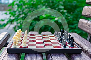 Chess pieces are placed on a chess board against a blurred background of nature. The pawns are black and white opposite