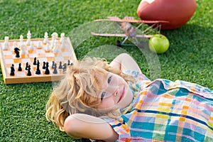 Chess school outdoor. Kid relax in park, laying on grass, daydreaming. Summer dream. Kid dreams on grass. Childhood