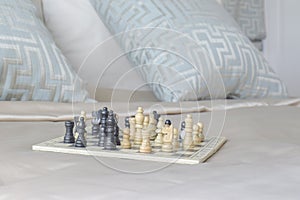 Chess set on satin bedding with light blue pillows in background