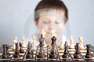 A chessboard with spaced figures, in the background a boy out of focus. Board game of chess. Tournaments and schools for young