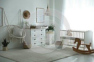 Chest of drawers with changing tray and pad near cradle in baby room. Interior design