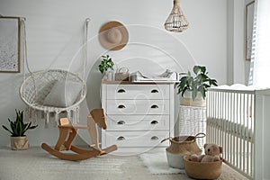 Chest of drawers with changing tray and pad near cradle in baby room. Interior design