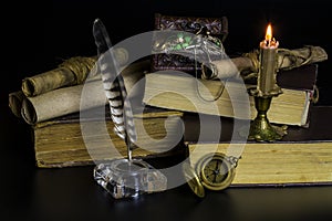 The chest with jewelry, old documents in scrolls and books, a burning candle and a compass on a black background