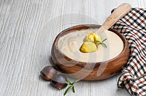 Chestnut cream soup in wooden bowl on white wooden table