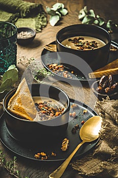 Chestnut soup with rosted topping, cream and bread in a black bowl on rustic wooden background