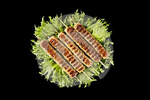 Chevapchichi, meat appetizer on a black background. Lettuce leaves complement the meat dish. Lula-Kebab. Selective focus