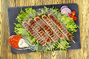 Chevapchichi, meat appetizer with sauce on a stone board. Lettuce leaves and hot pepper complement the meat dish. Lula-Kebab.