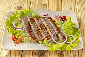 Chevapchichi, a meat appetizer on a wooden table. Lettuce leaves and hot pepper complement the meat dish. Lula-Kebab. Selective