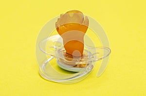 A chewed baby pacifier on a yellow background. Concept of teething in children, close-up.