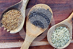 Chia, flax, and hemp seeds on the wooden background.