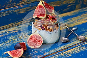 Chia milk pudding with granola and fresh sliced figs in the glass jar decorated with vintage spoons on the blue wooden table