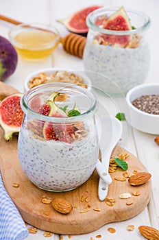 Chia pudding with yogurt, homemade granola, fresh figs and honey in a glass jar on a board