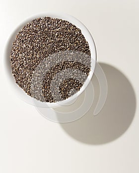 Chia Seed. Grains in a bowl. Shadow over white table.