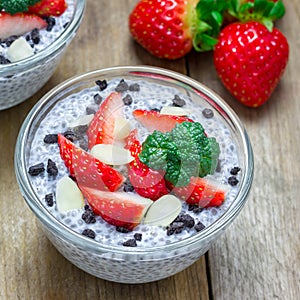 Chia seed pudding with strawberries, almond and chocolate cookie crumbs, on wooden table, square format