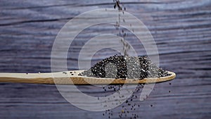 Chia seeds falling into a wooden spoon on gray background