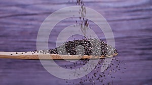 Chia seeds falling into a wooden spoon on gray background