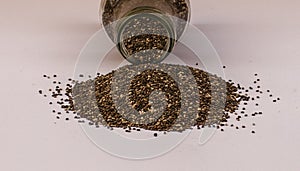 Chia seeds spilling of glass jar on white background