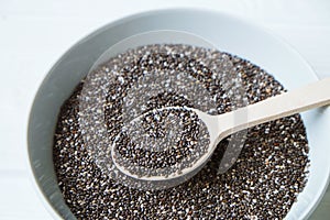 Chia seeds in a wooden spoon in a bowl on the table close-up.