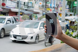 CHIANG MAI,THAILAND - JULY 17, 2016 : A man hand holding Uber app showing on LG G4 on road and red car, Uber is smartphone app-ba