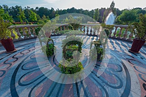 A chic composition of chairs and a table panned by green plants standing on a round platform paved with patterned tiles