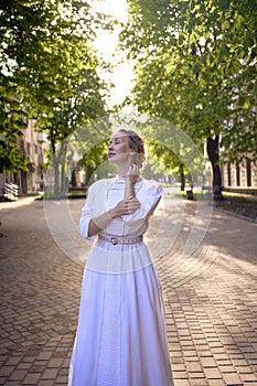 chic middle age woman in a white vintage dress in a sunlit alley