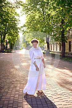 chic middle age woman in a white vintage dress in a sunlit alley