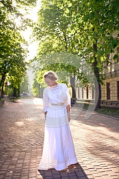chic middle age woman in a white vintage dress in a sunlit alley