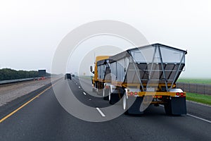 Chic new yellow truck with two bulk trailers on straight as arrow highway in fog