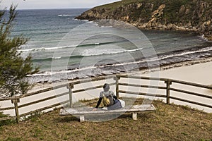 Chica senderista descansa en un banco y disfruta de la vista panoramica de la playa de esteiro en la ruta de los faros photo