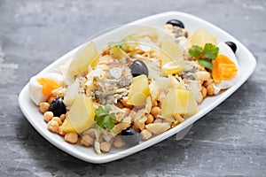 Chick peas with cod fish, olives and boiled egg in white dish on ceramic background