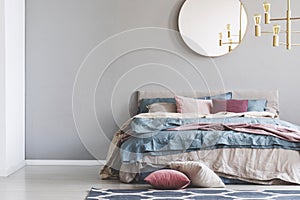 Chick round mirror on grey empty copy space wall in elegant bedroom interior with warm bed with blue, pastel pink and beige