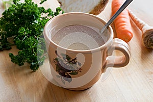 Chicken bone broth in a mug with vegetables in the background