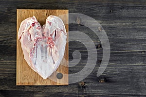 Chicken breast bones up lies on a bamboo cutting Board on a wooden rustic dark background