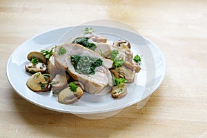 Chicken breast fillet stuffed with spinach, served with mushrooms and parsley garnish on a light wooden table with copy space