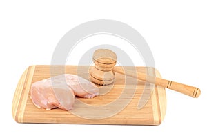 Chicken breast and meat mallet on wooden platter.