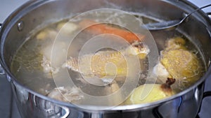 Chicken broth is cooked on a gas stove, the cook collects fat