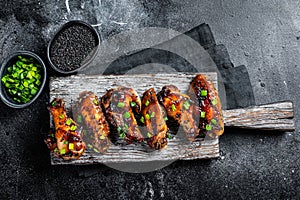 Chicken buffalo wings in sweet and sour sauce with black sesame. Black background. Top view