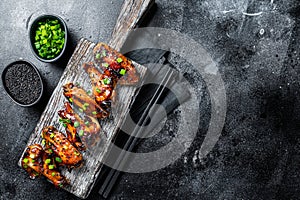 Chicken buffalo wings in sweet and sour sauce with black sesame. Black background. Top view. Copy space