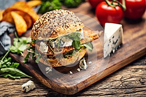 Chicken burger with blue cheese and arugula in a sesame bun on a rustic wood