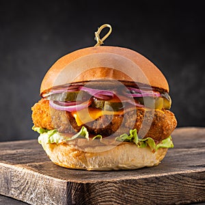Chicken burger with cheese and pickles on a wooden board