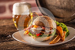Chicken burger with fried egg and bacon, salad, peppers and potato wedges served on a plate next to a draft beer