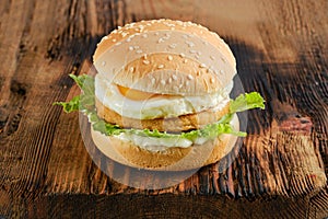 Chicken burger with fried egg and iceberg lettuce on wooden board