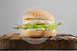 Chicken burger with fried egg and iceberg lettuce on wooden board, front view