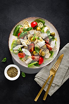 Chicken Caprese pasta salad with mozzarella cheese, olives, tomato and fresh basil. Top view, flat lay