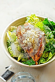 Chicken Ceasar salad. Cos lettuce leaves, grilled chicken breast sliced, parmesan cheese. Restaurant table