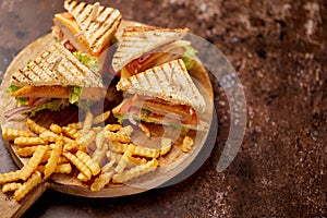 Chicken and cheese club sandwiches served on a wooden board with french fries