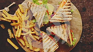 Chicken and cheese club sandwiches served on a wooden board with french fries